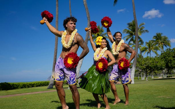 Performers at a Kaula-Luau in Hawaii, wearing traditional attire and holding feathered gourd rattles.
