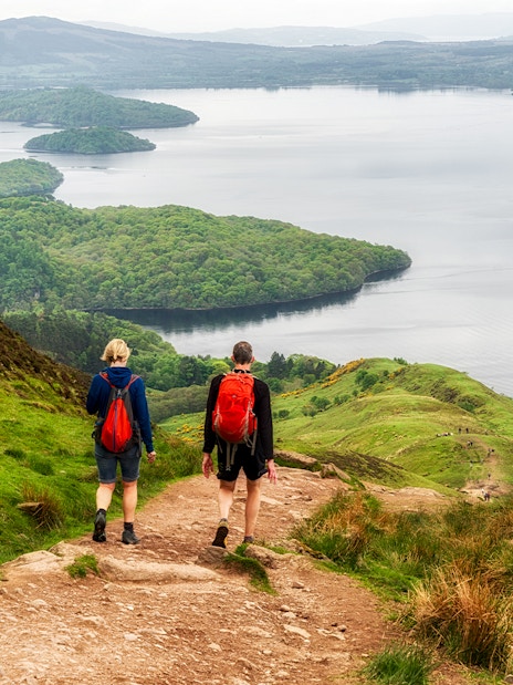 Hikers on a trail overlooking a loch in the Scottish Highlands.