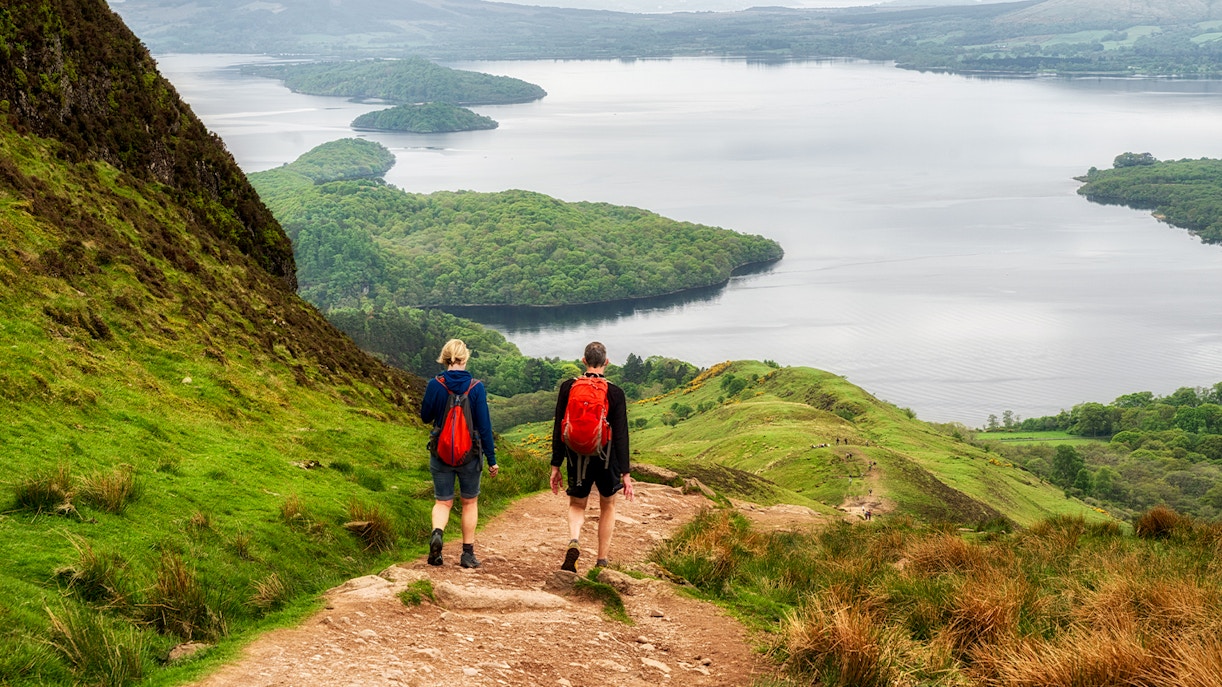 Hikers on a trail overlooking a loch in the Scottish Highlands.