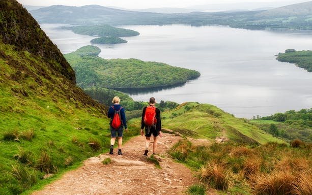 Hikers on a trail overlooking a loch in the Scottish Highlands.