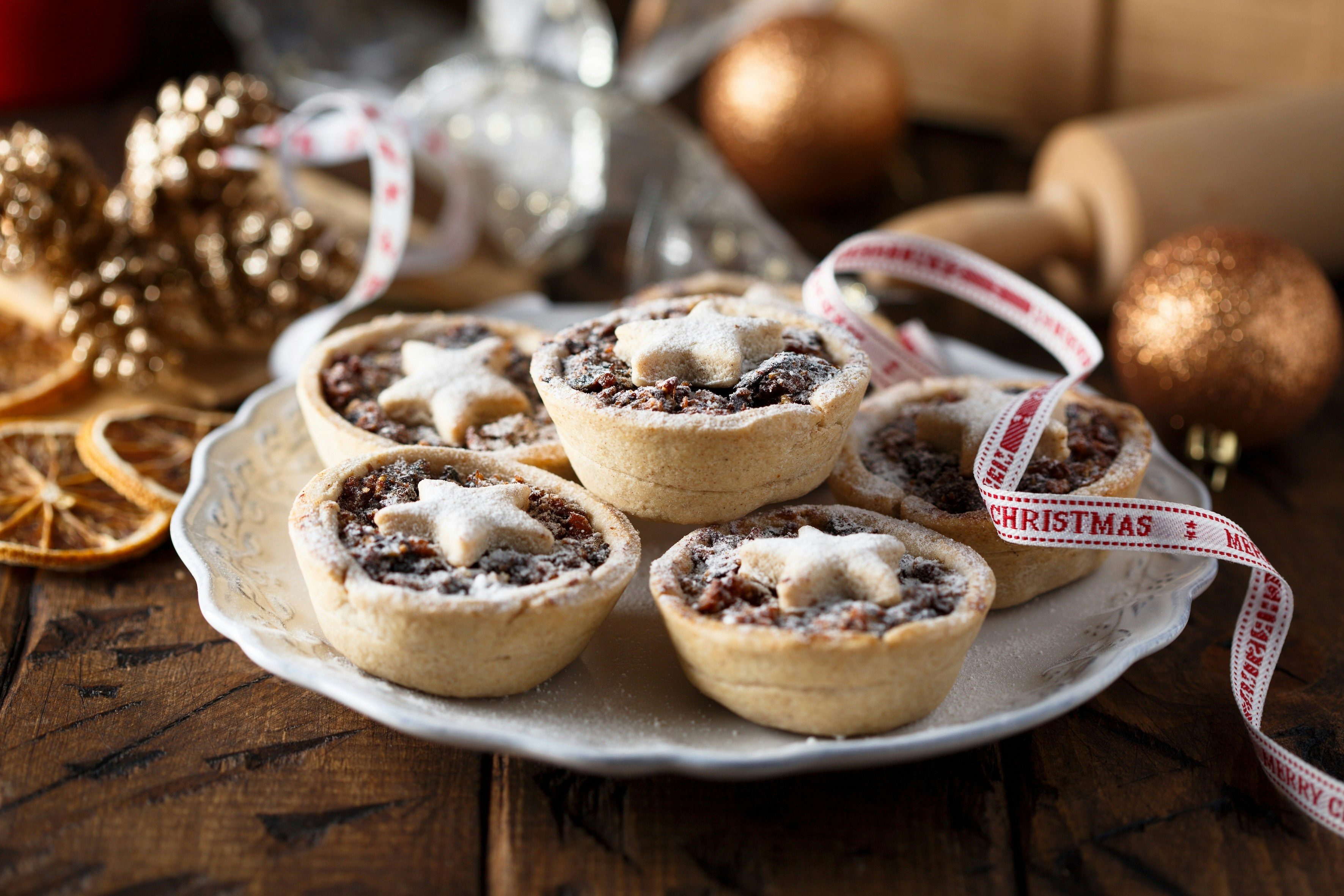 Mince pies with star tops on a white plate, surrounded by festive decorations.