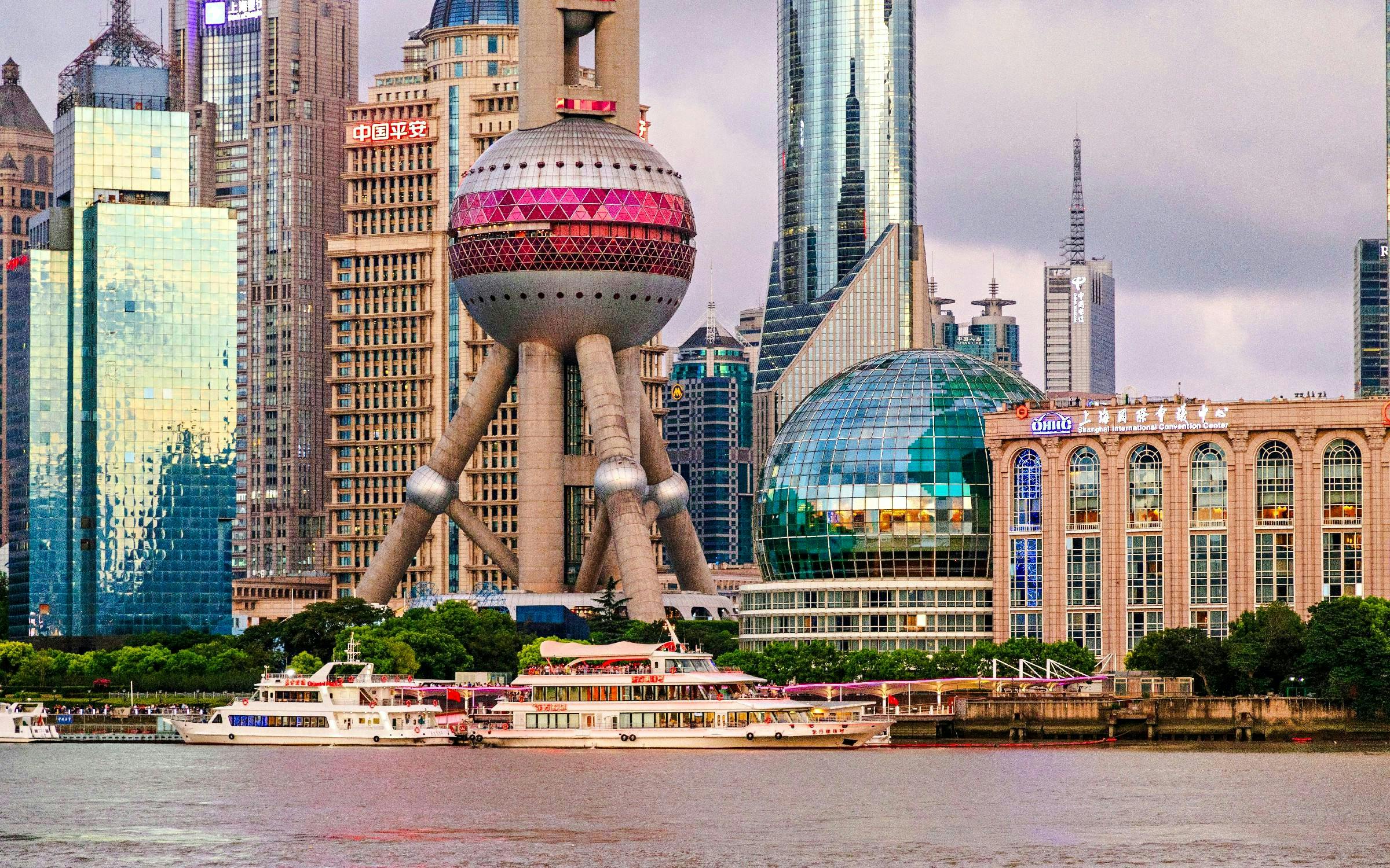 Oriental Pearl Tower in Shanghai's Pudong district with nearby skyscrapers and riverboats.