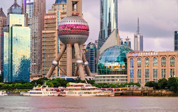 Oriental Pearl Tower in Shanghai's Pudong district with nearby skyscrapers and riverboats.