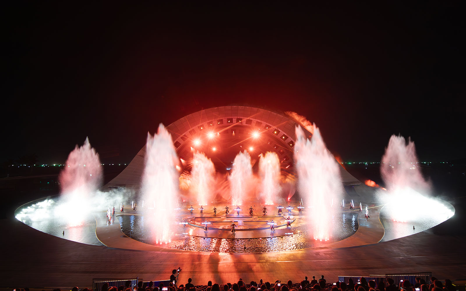 Fountain and light display at Kiss of the Sea Show, featuring performers on stage.