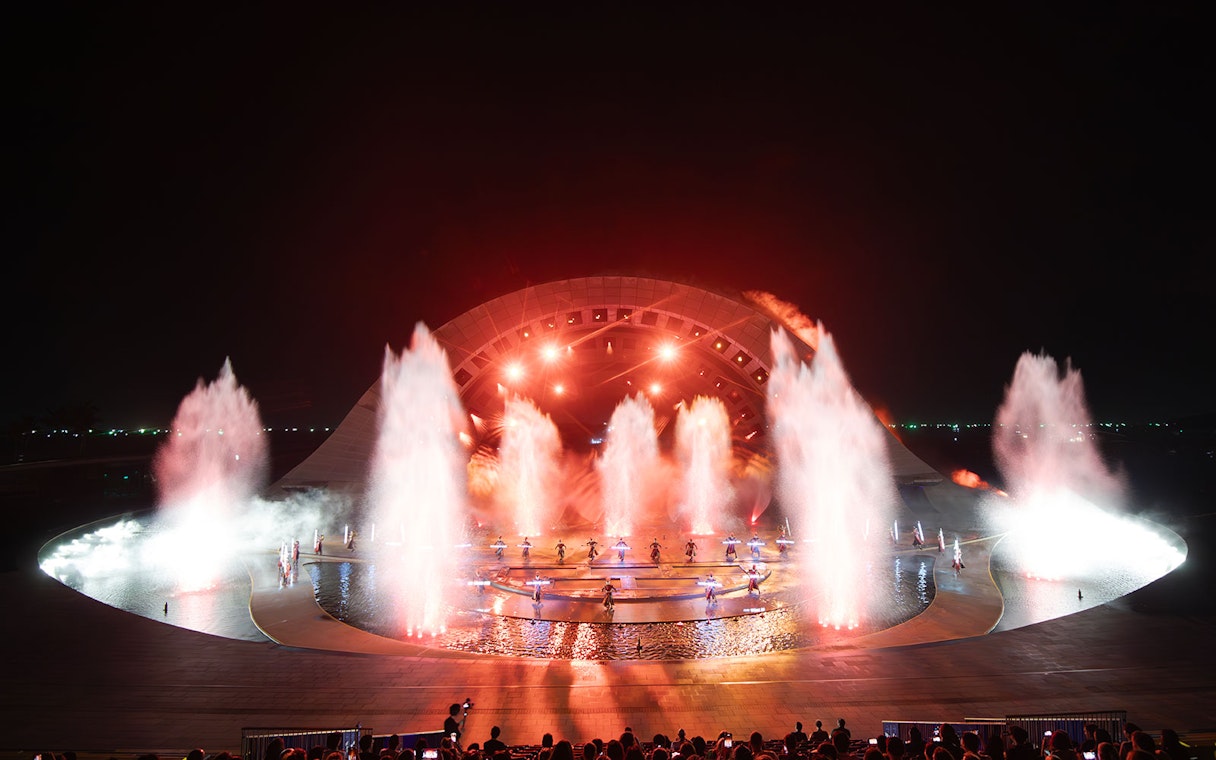Fountain and light display at Kiss of the Sea Show, featuring performers on stage.