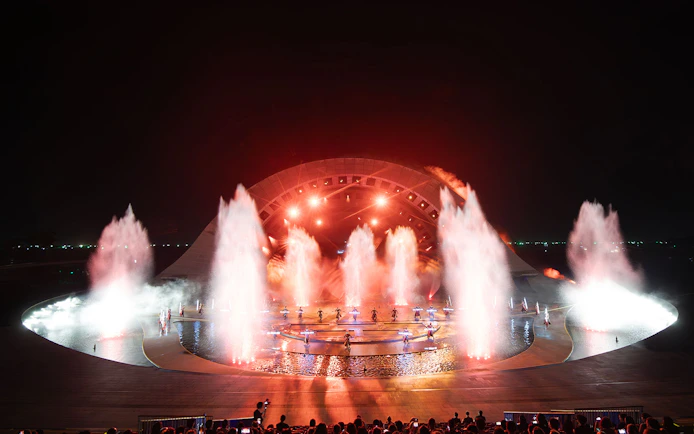 Fountain and light display at Kiss of the Sea Show, featuring performers on stage.