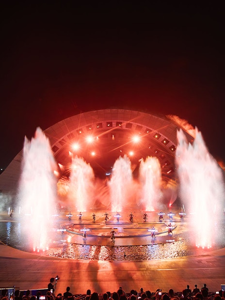 Fountain and light display at Kiss of the Sea Show, featuring performers on stage.