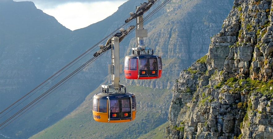 Cable cars ascending Table Mountain, Cape Town, with rocky cliffs in the background.