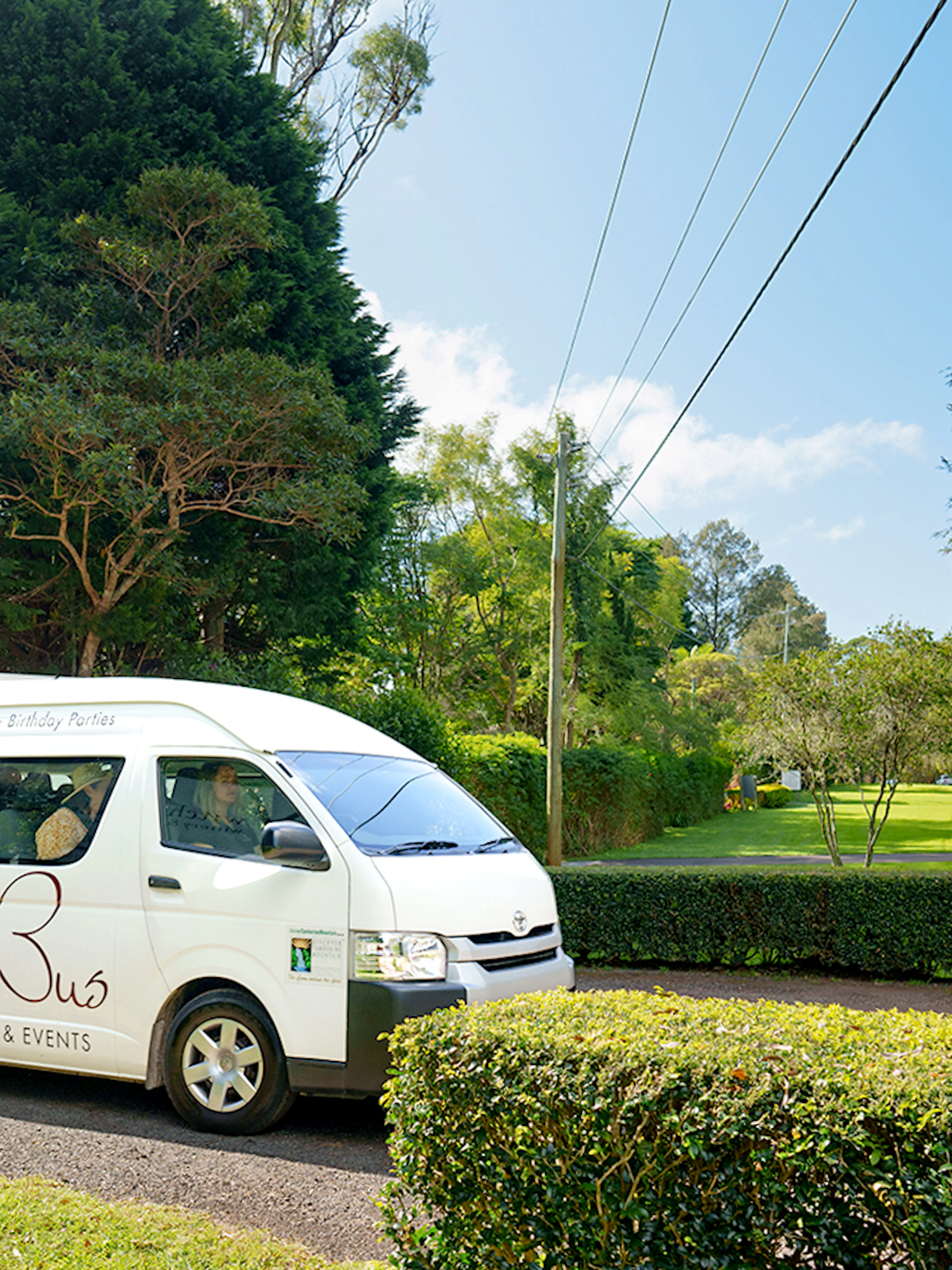 Winery tour bus on scenic road near Brisbane, surrounded by lush greenery.