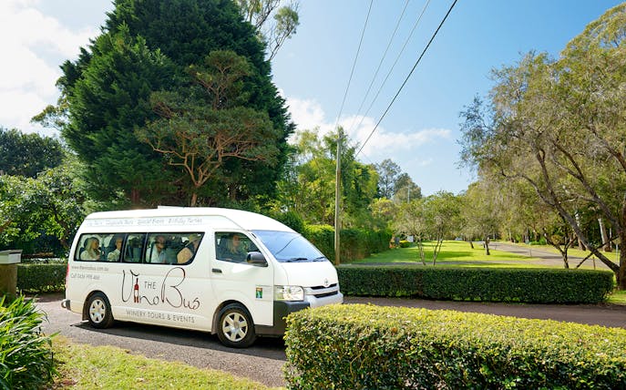 Winery tour bus on scenic road near Brisbane, surrounded by lush greenery.