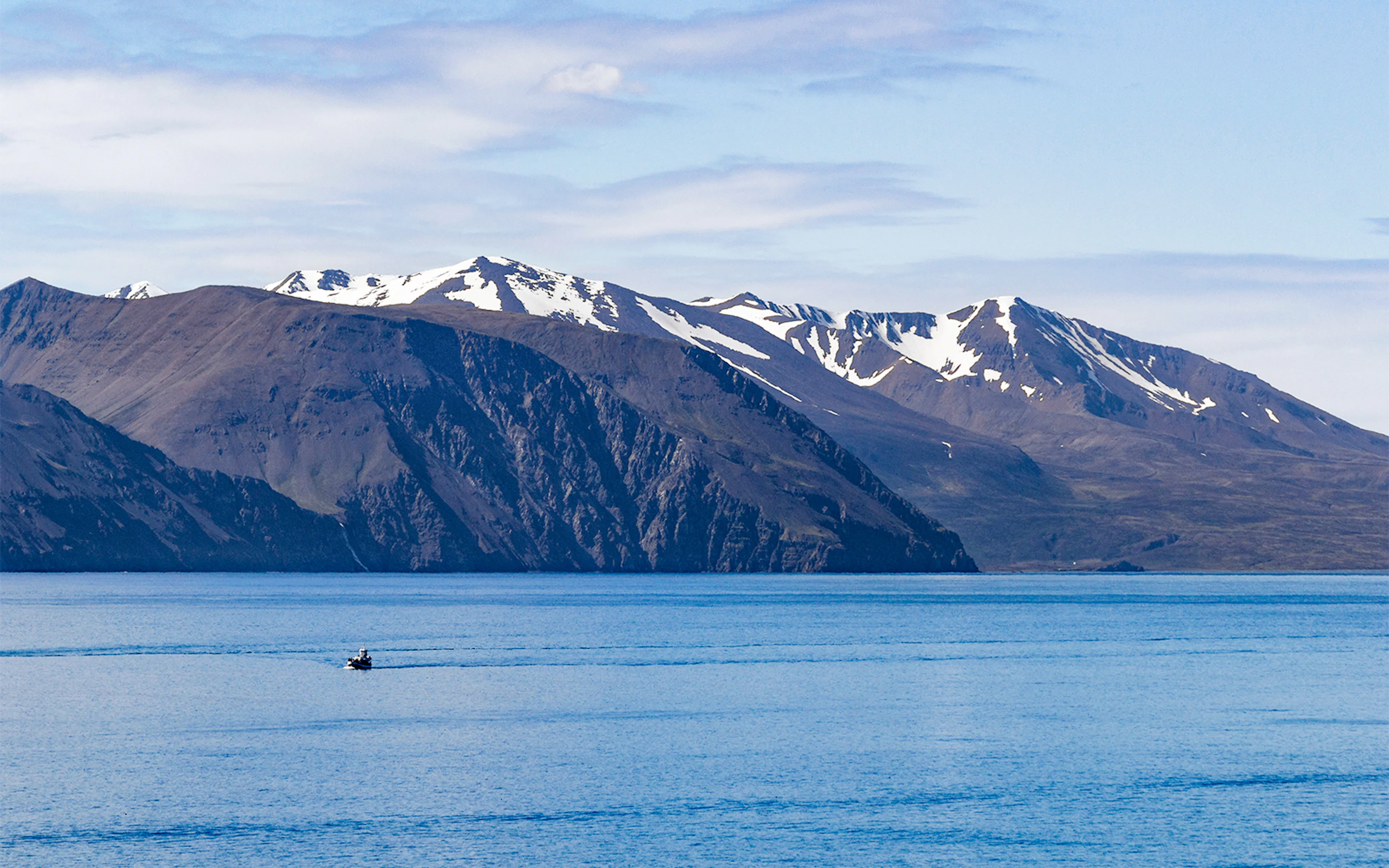 Boat on Bay of Skjálfandi with snow-capped mountains in Iceland.