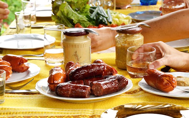 Sausages and condiments on a table set for a bonfire meal.