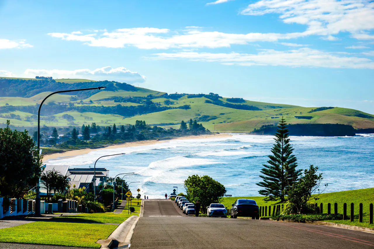 Coastal road leading to Kiama Blowhole with ocean waves and green hills in Sydney.