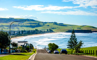 Coastal road leading to Kiama Blowhole with ocean waves and green hills in Sydney.