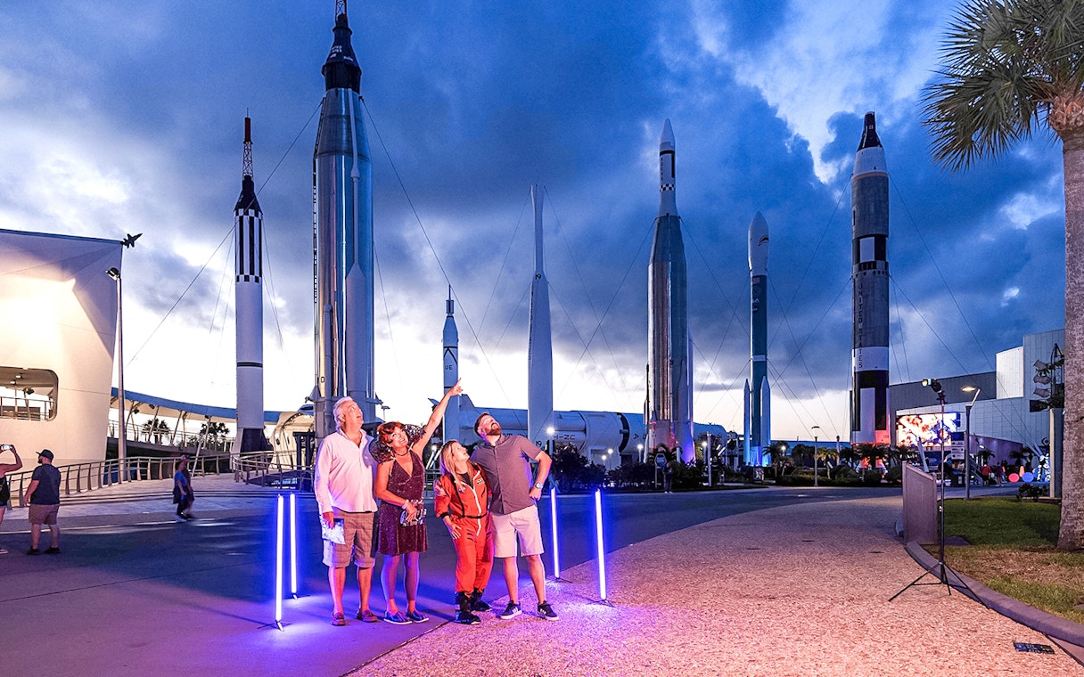 Visitors at Kennedy Space Center under rockets during exclusive after-hours event.