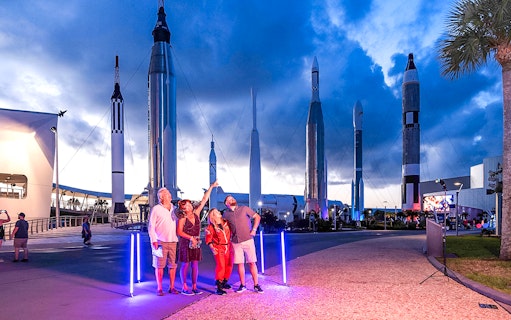 Visitors at Kennedy Space Center under rockets during exclusive after-hours event.