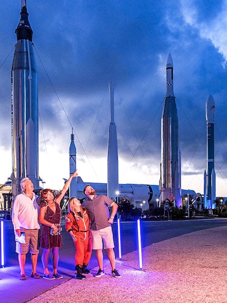 Visitors at Kennedy Space Center under rockets during exclusive after-hours event.