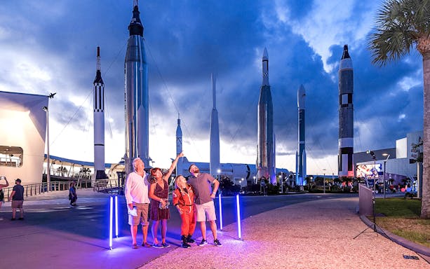 Visitors at Kennedy Space Center under rockets during exclusive after-hours event.