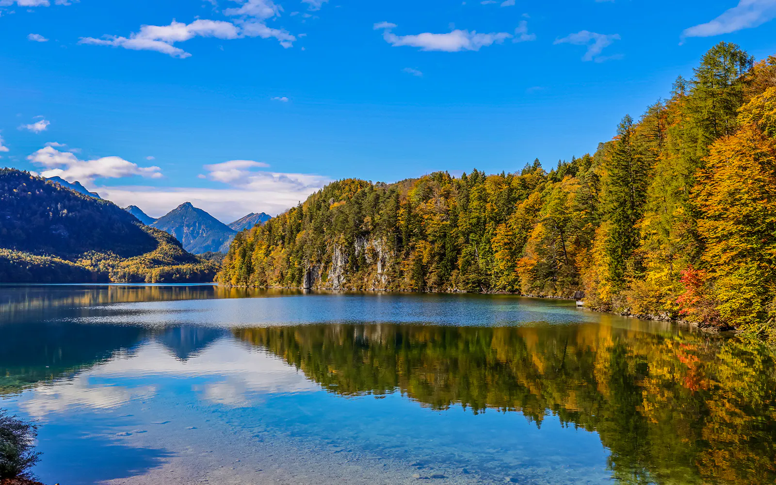 Lake Alpsee with autumn trees and mountain backdrop near Neuschwanstein Castle, Germany.