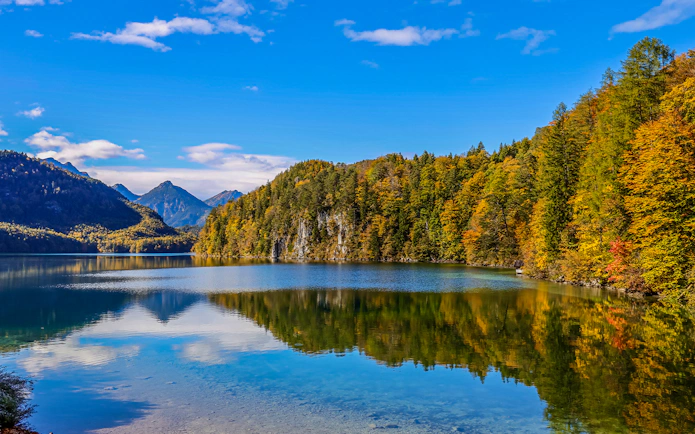 Lake Alpsee with autumn trees and mountain backdrop near Neuschwanstein Castle, Germany.