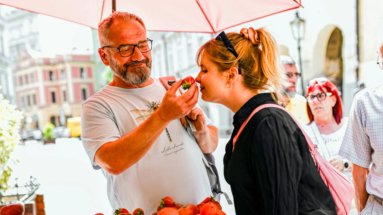 Man offering strawberry to woman at Prague market during Czech cuisine tour.