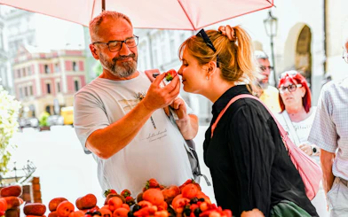 Man offering strawberry to woman at Prague market during Czech cuisine tour.