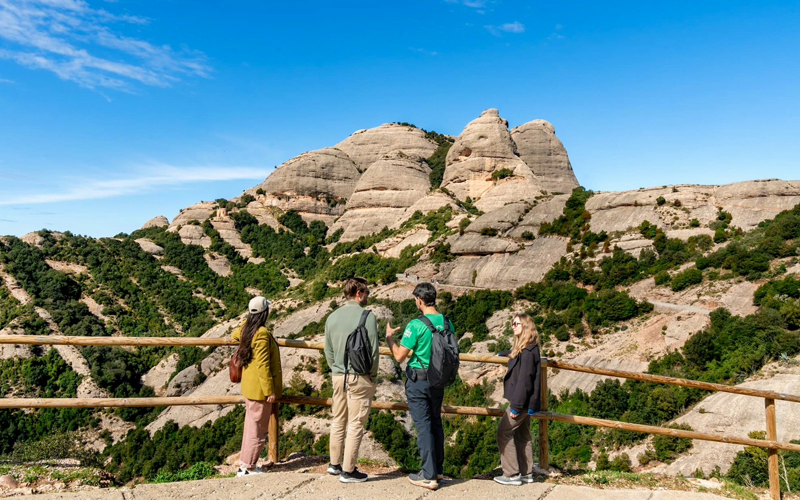 Tourists with guide at Montserrat mountain viewpoint, Spain, admiring rocky landscape.