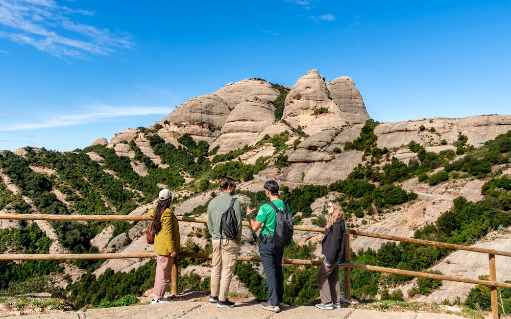 Tourists with guide at Montserrat mountain viewpoint, Spain, admiring rocky landscape.
