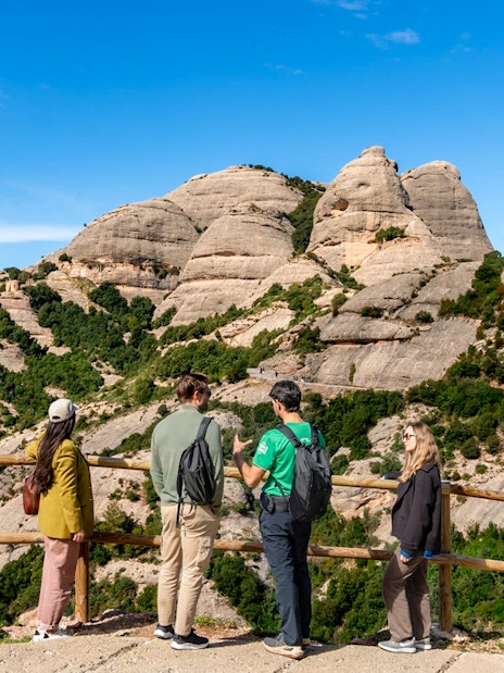 Tourists with guide at Montserrat mountain viewpoint, Spain, admiring rocky landscape.