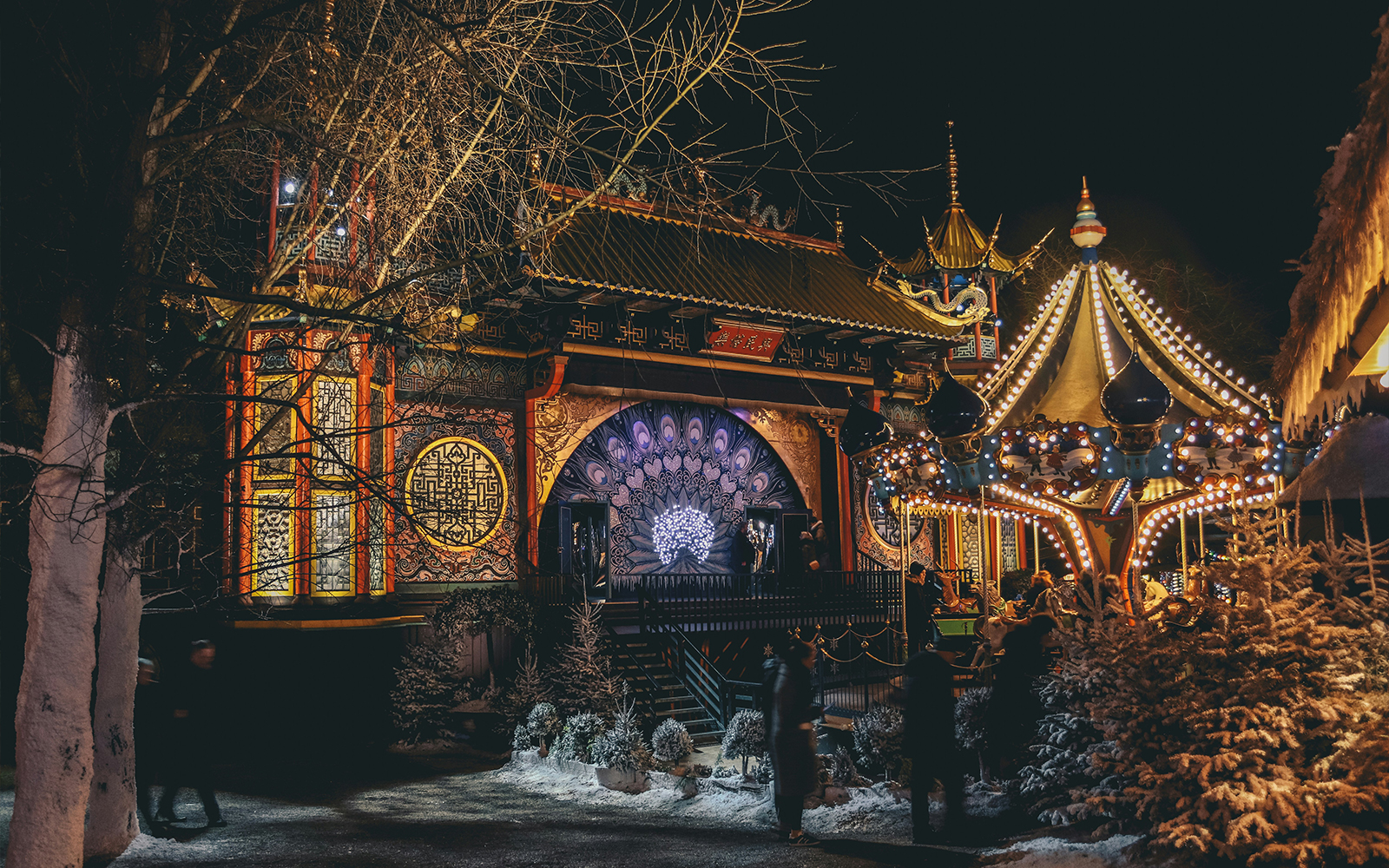 Tivoli Gardens at night with illuminated carousel and ornate building in Copenhagen.