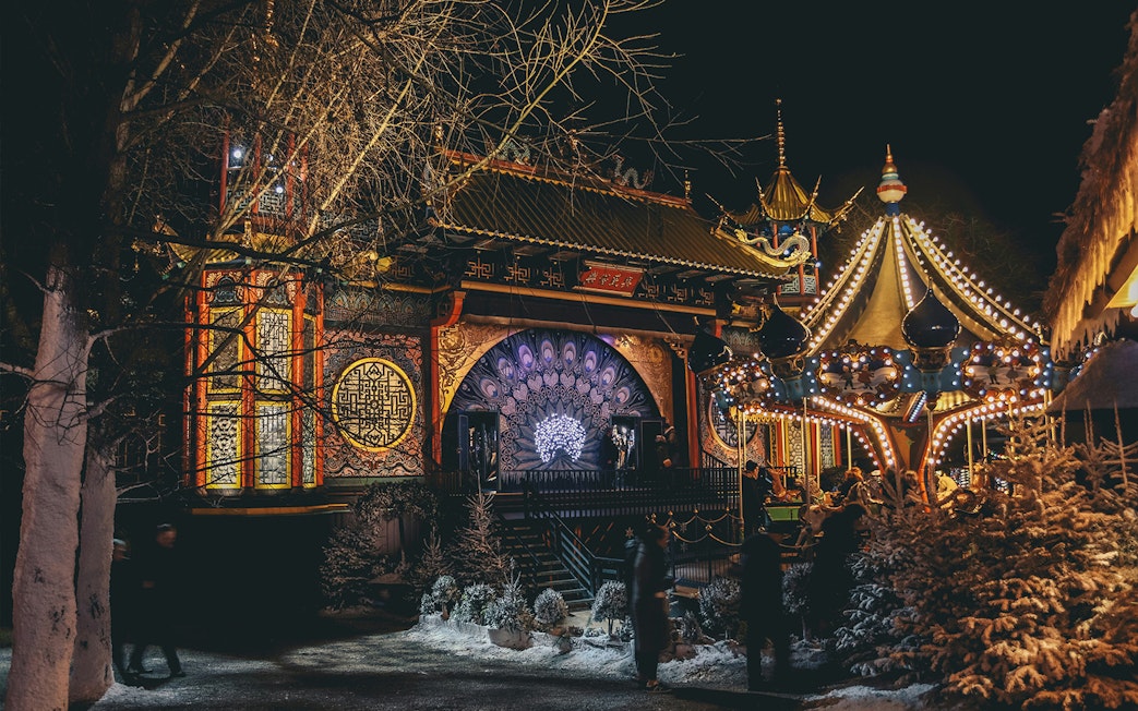 Tivoli Gardens at night with illuminated carousel and ornate building in Copenhagen.