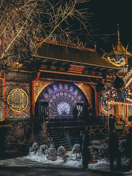Tivoli Gardens at night with illuminated carousel and ornate building in Copenhagen.