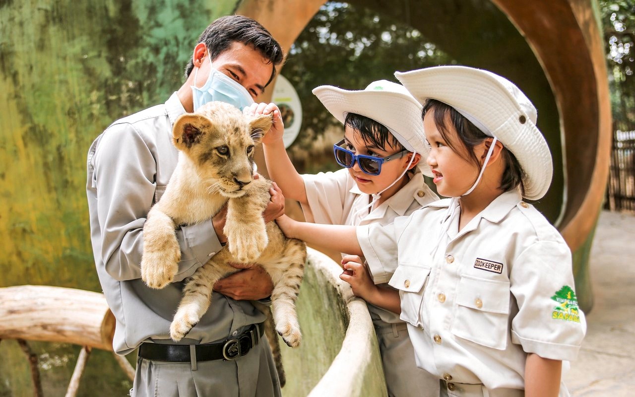 Kids petting lion cub at Vinpearl Safari with zookeeper.
