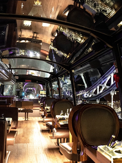 Interior of a glass-roofed bus with dining tables, showcasing London city lights on the Bustronome tour.