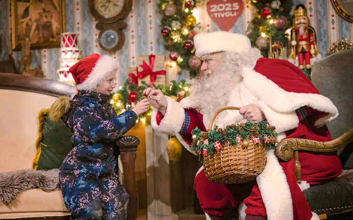 Santa Claus giving a gift to a child inside Tivoli Gardens, Copenhagen during Christmas.