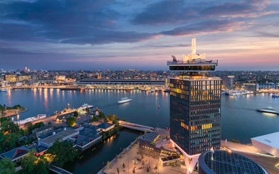 A'DAM Lookout tower overlooking Amsterdam cityscape and river at sunset.