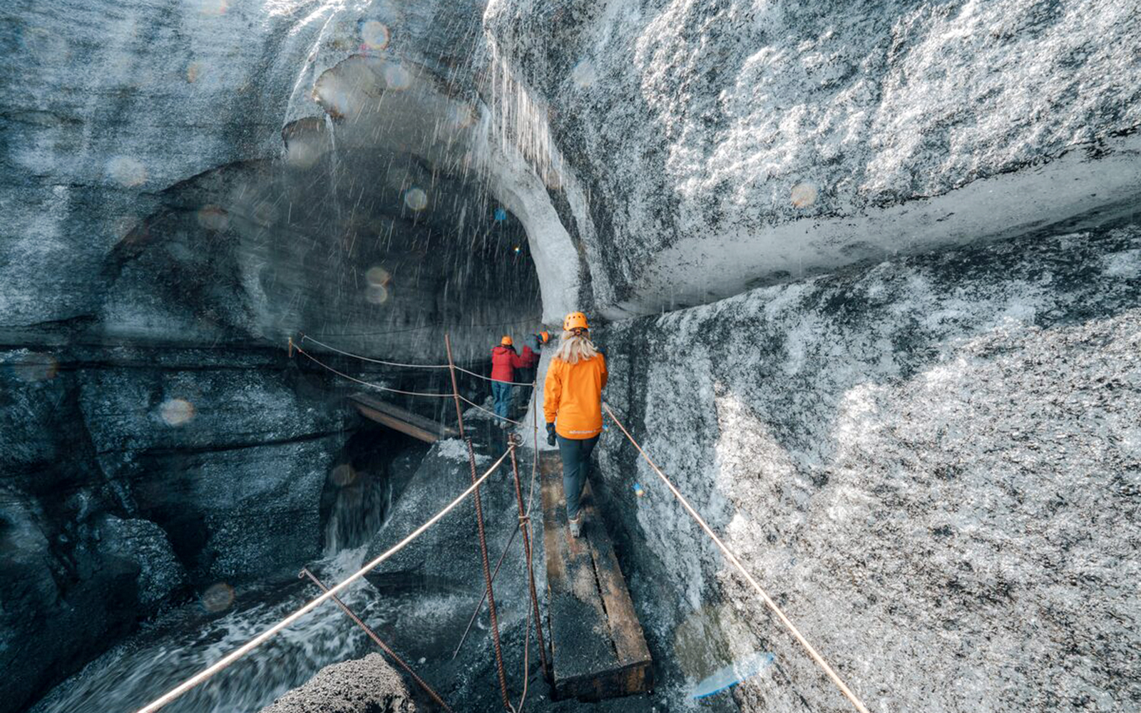 Tour guide assisting guests on a narrow path inside Katla Ice Cave, Iceland.