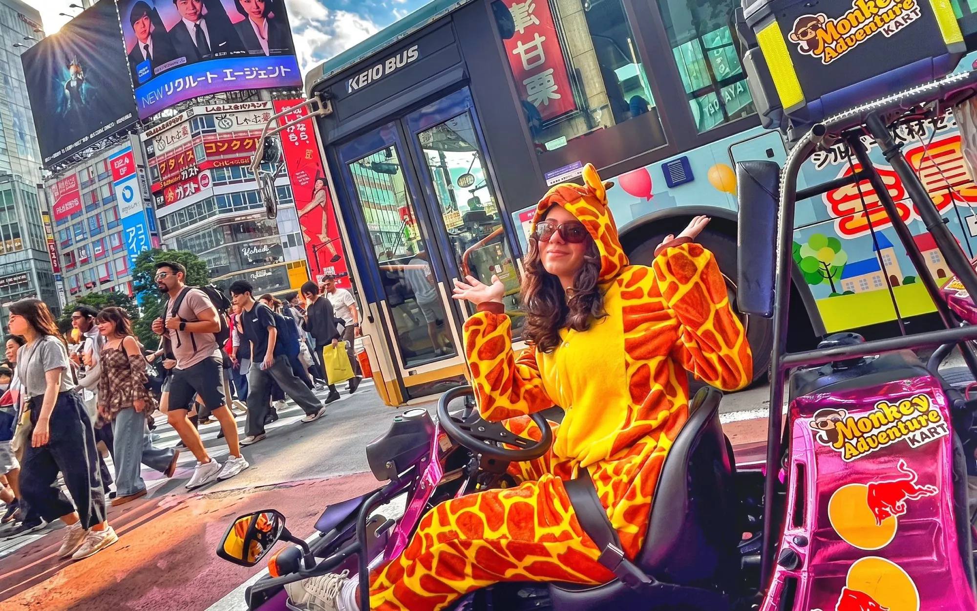 Person in giraffe costume sitting in go-kart at Shibuya Crossing, Tokyo, with busy street scene.