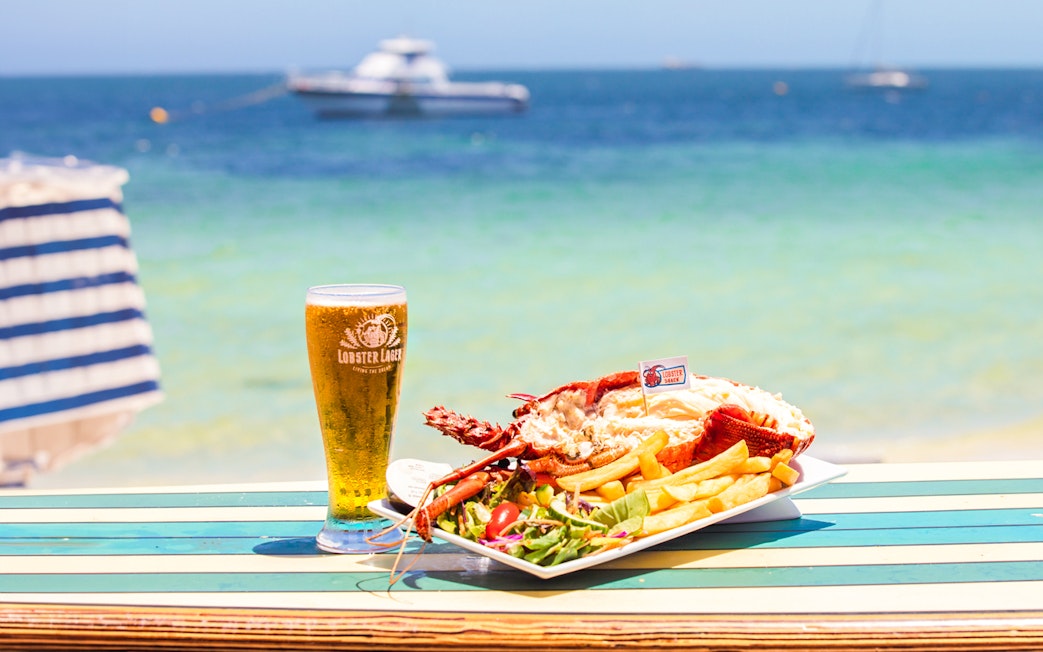 Lobster meal with fries and salad on a beachside table in Australia, with a glass of beer.