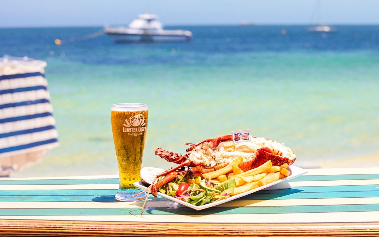 Lobster meal with fries and salad on a beachside table in Australia, with a glass of beer.
