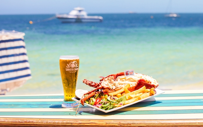 Lobster meal with fries and salad on a beachside table in Australia, with a glass of beer.