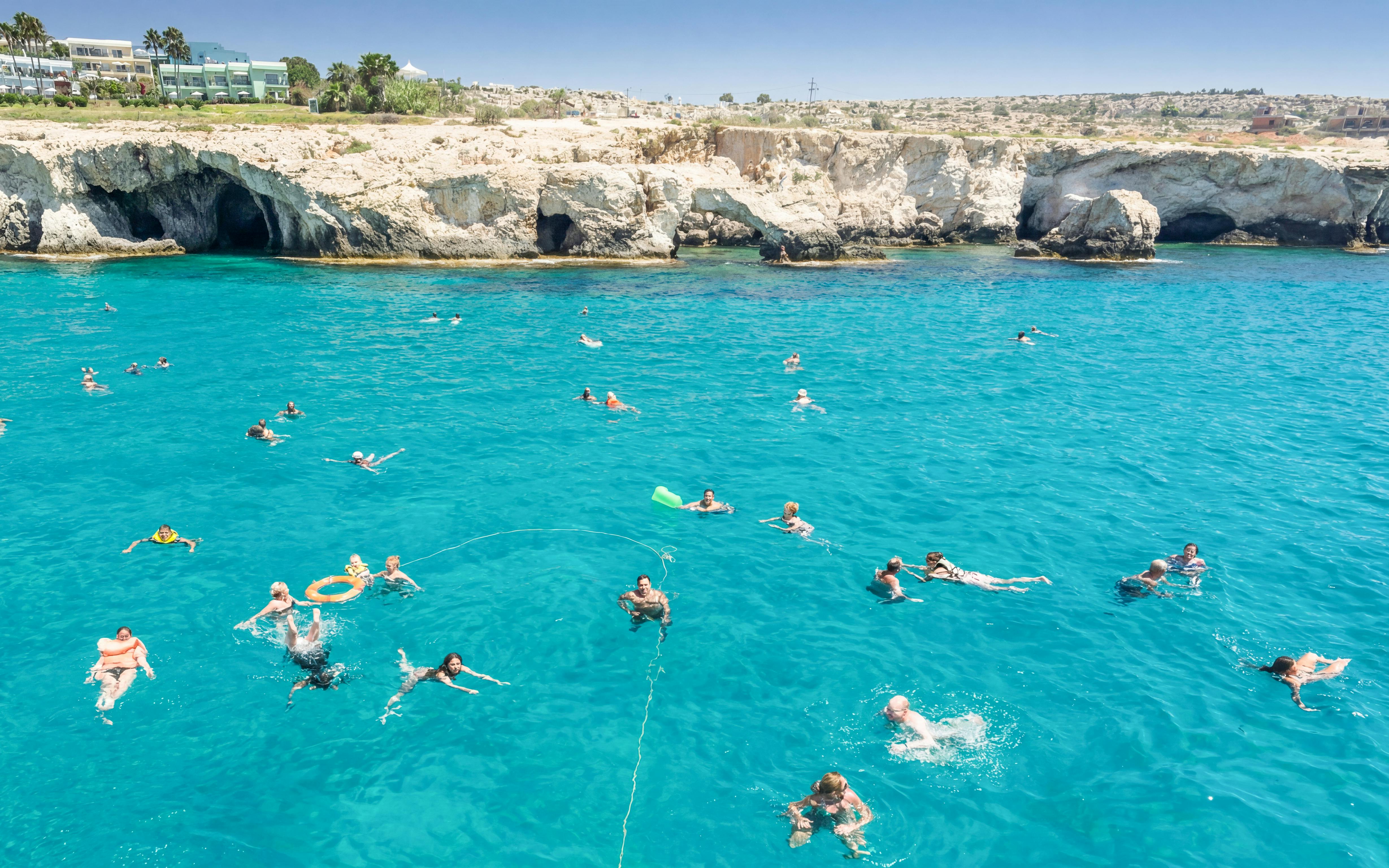 People swimming in the clear blue waters of Blue Lagoon, Cyprus, near rocky cliffs.