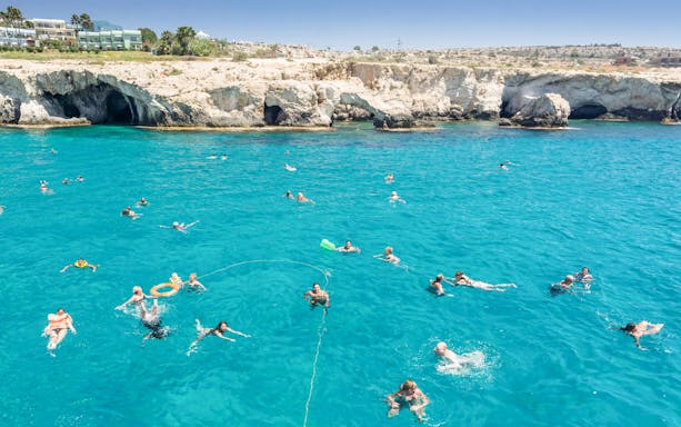 People swimming in the clear blue waters of Blue Lagoon, Cyprus, near rocky cliffs.