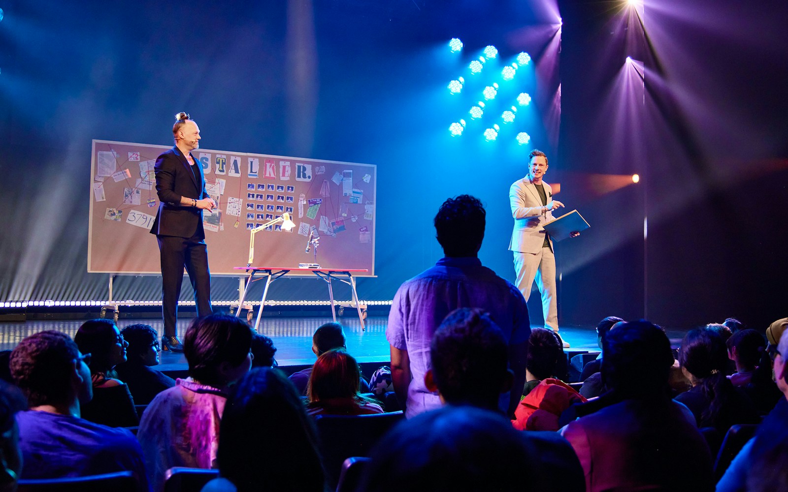 Audience watching a live stage performance with a board labeled "Stalker" in the background.