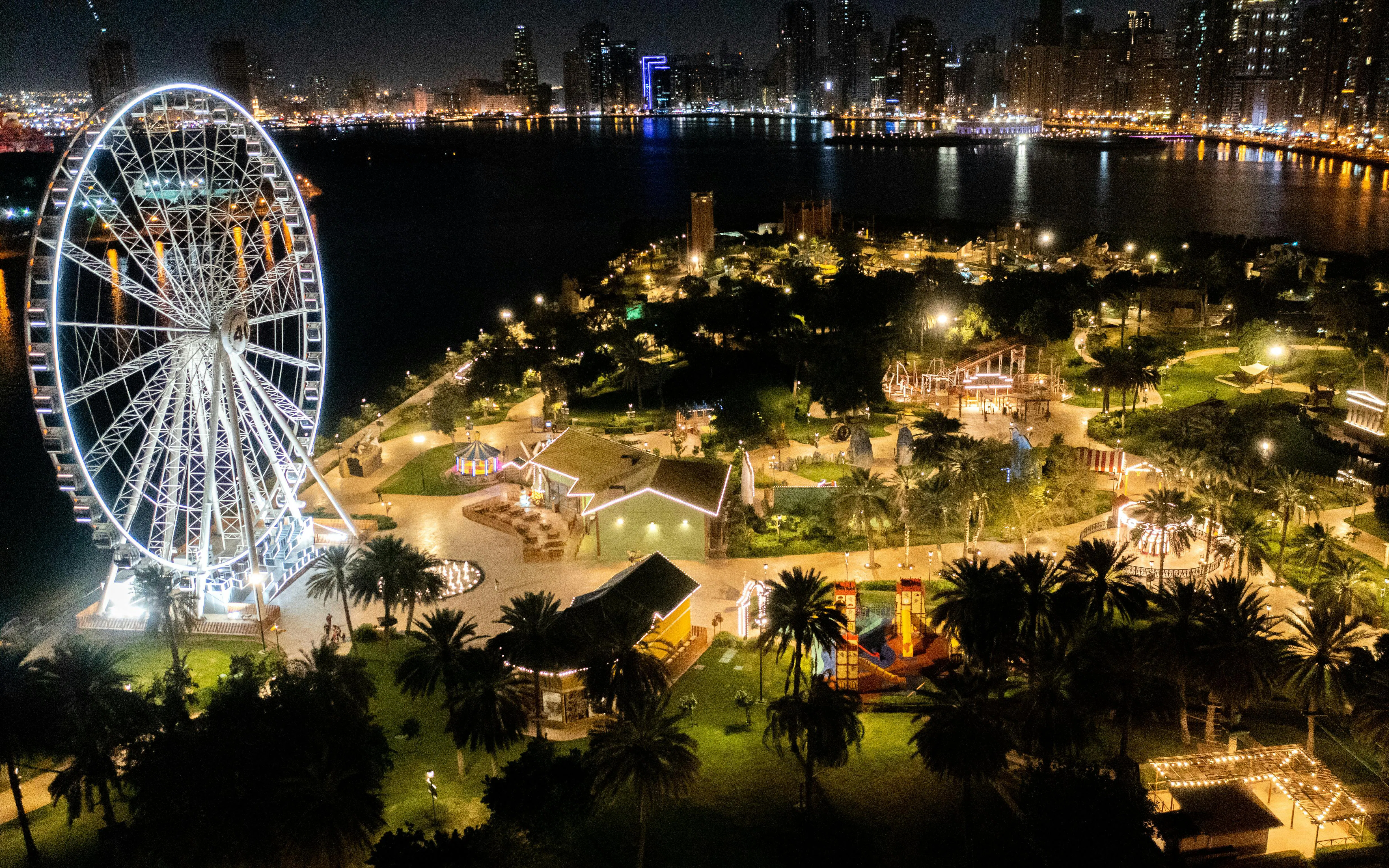 Ferris wheel and illuminated attractions at Al Montazah Parks, Island of Legends, Sharjah at night.