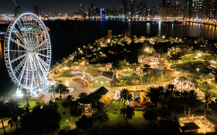 Ferris wheel and illuminated attractions at Al Montazah Parks, Island of Legends, Sharjah at night.