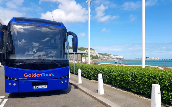 AC coach parked near coastal road with sea and cliffs in the background.