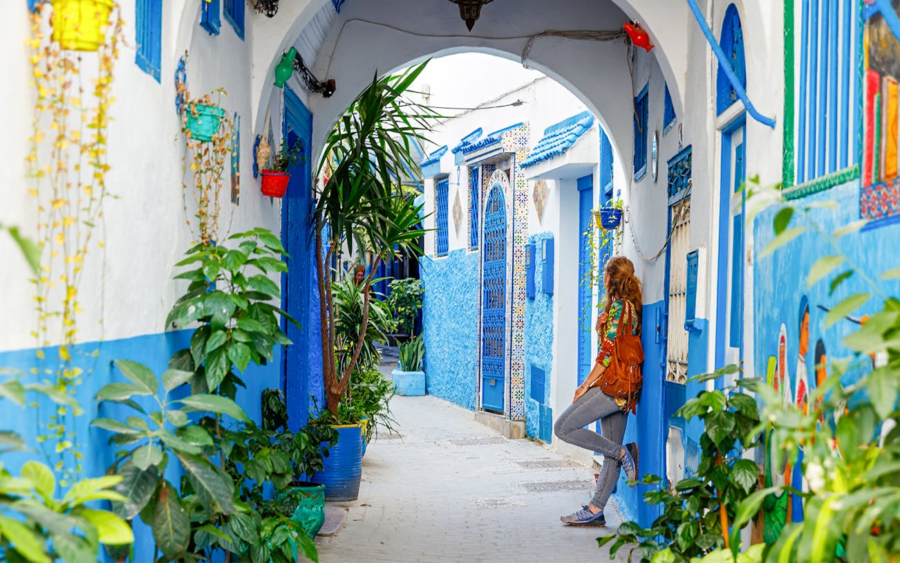 Colorful alley in Tangier with blue and white buildings, plants, and a person exploring.