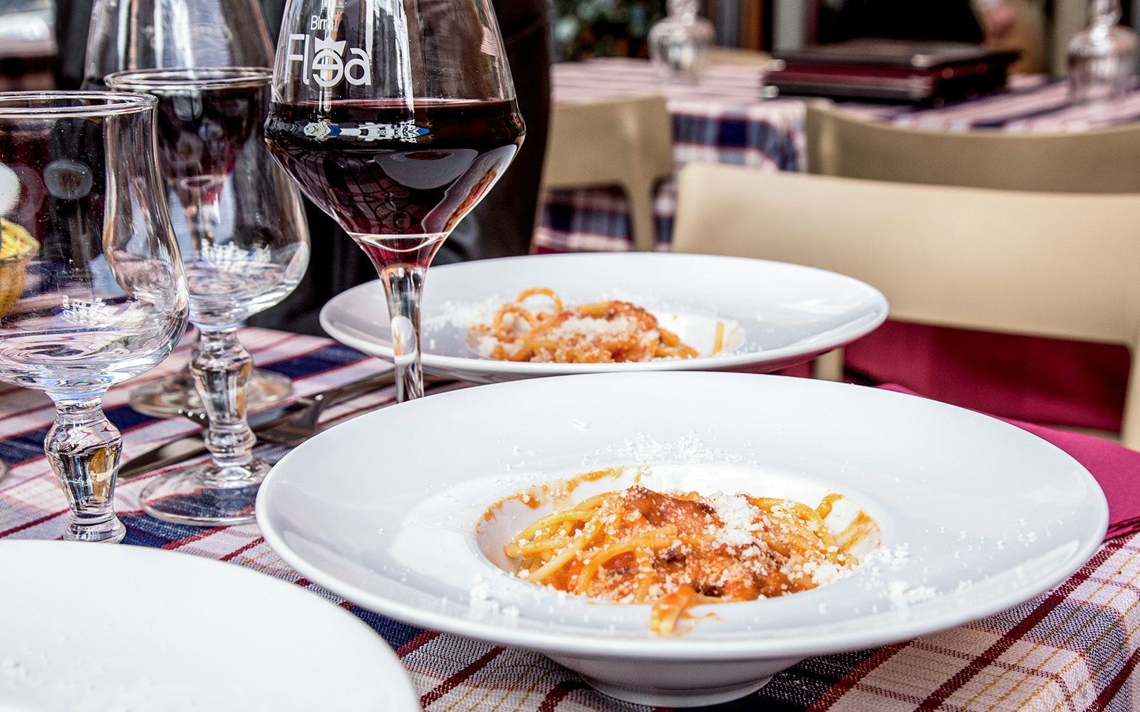 Italian pasta with tomato sauce and cheese served on a table with wine glasses in a restaurant.