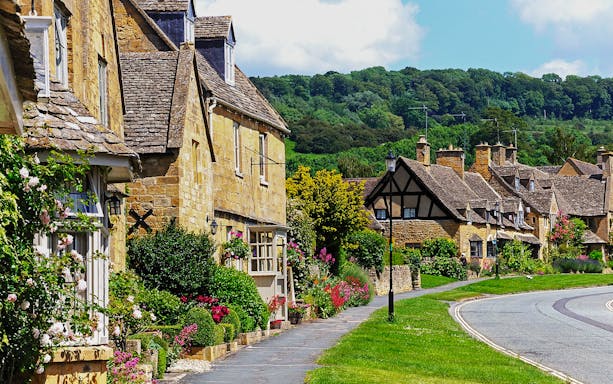 Cotswolds village street with stone cottages and lush gardens.